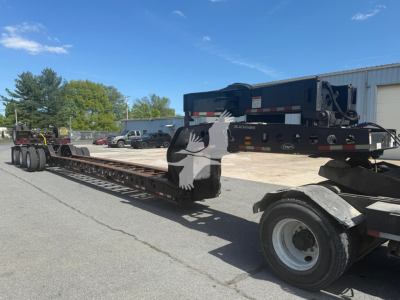 Lowboy trailer with Etnyre beam and hydraulic equipment. Side shows long deck with multiple axles, tag and warning decals. No legible fine print visible in this view.