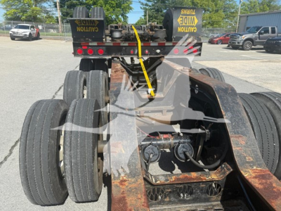 ETNYRE beam lowboy trailer rear view showing dual rear axles with six wheels, rusted steel frame, and hydraulic lines; warning straps on top and clearance lights.