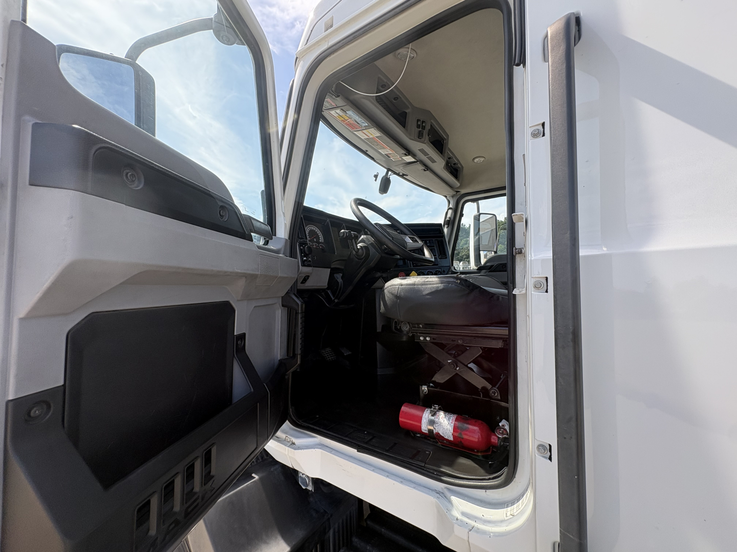 Cab interior of a 2022 Mack AN42T with driver door open, steering wheel visible, dashboard and seat, fire extinguisher on floor near door.