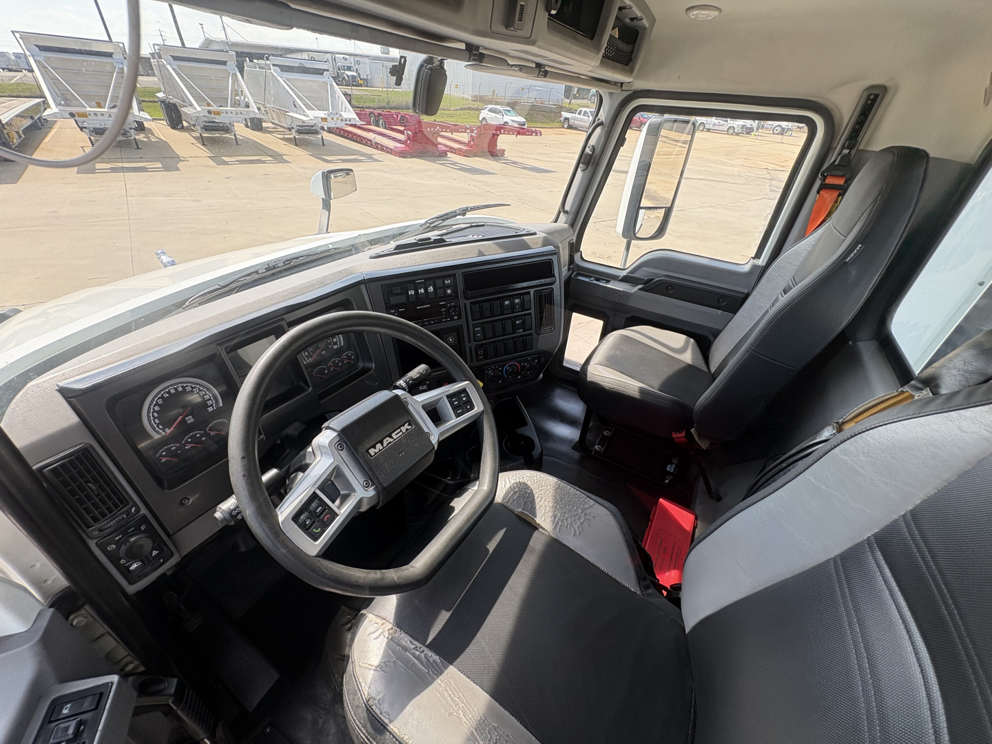 Truck cabin front dashboard and steering wheel view of a 2022 Mack AN42T daycab from the passenger side showing steering wheel, gauges, and driver seat.
