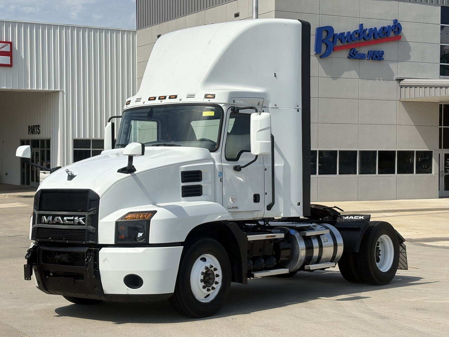 Truck image: 2022 Mack AN42T conventional daycab tractor, white with sleeper high roof, front grille with Mack badge, dual rear wheels, parked outside a dealership.