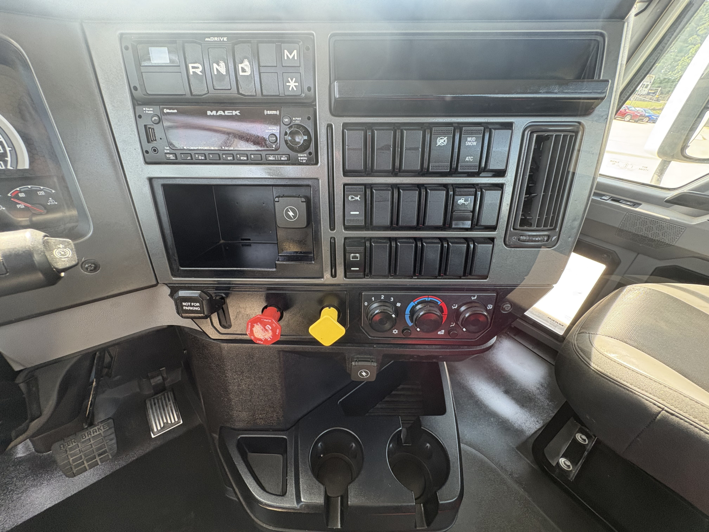Cab interior of a 2022 Mack AN42T showing dashboard controls, gear selector indicators R N D M, switches, climate controls, cup holders, and storage compartments.