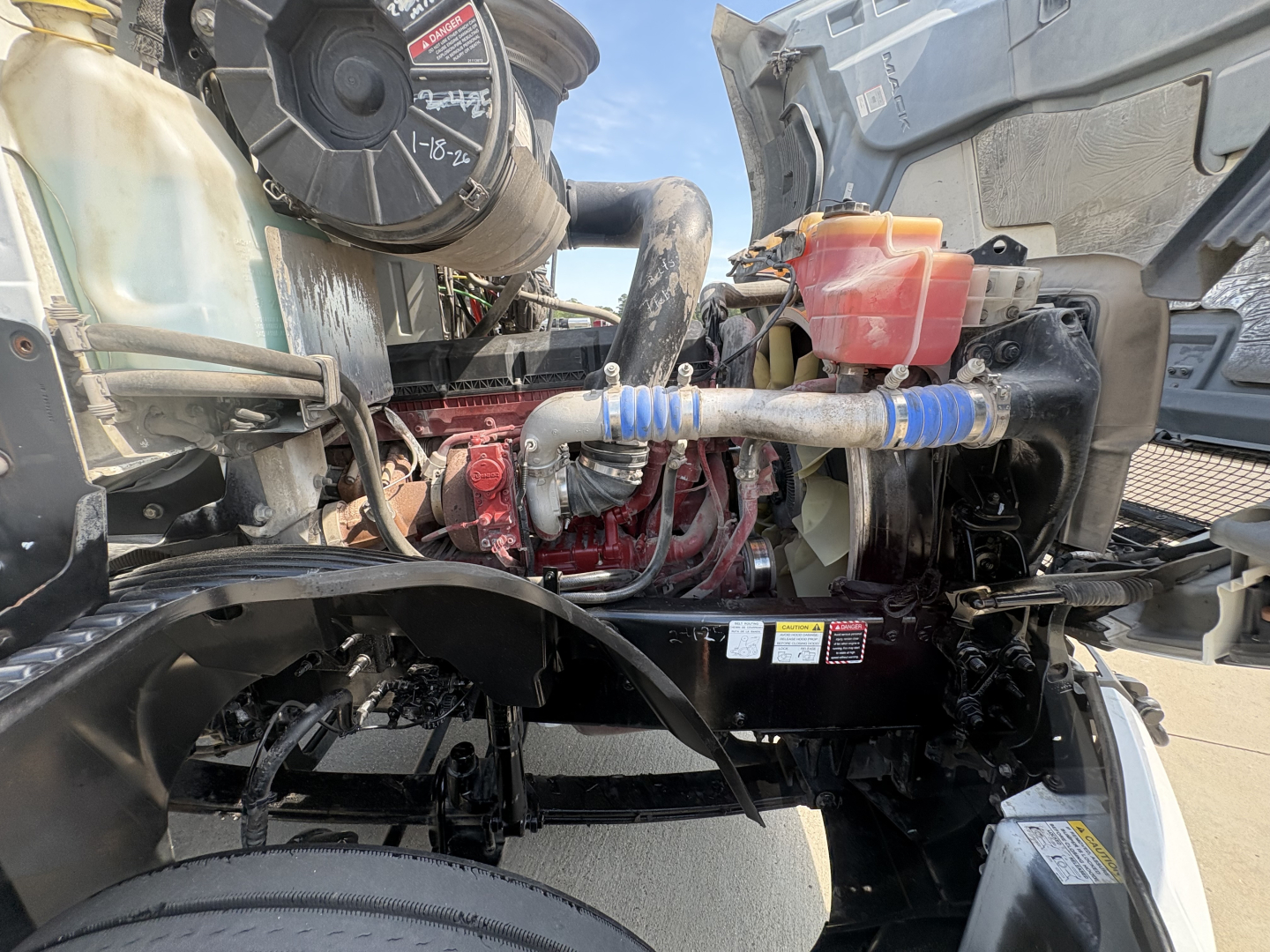 Engine bay of a 2022 Mack AN42T daycab showing coolant reservoir, hoses, and engine components with blue hose clamps.