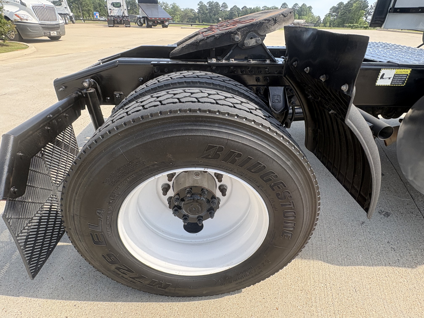Mack AN42T truck corner showing spare wheel and fender, Bridgestone tire with white rim, undercarriage components.