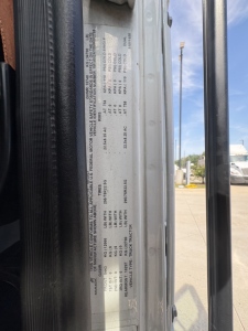 Truck cab door sticker with vehicle specifications and weights; text includes VIN, axle ratings, and model details. Side view of door jamb with labels and numbers visible.