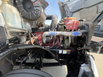 Engine bay of a 2022 Mack AN42T daycab showing coolant reservoir, hoses, and engine components with blue hose clamps.