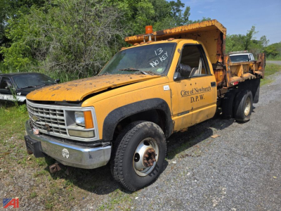Chevrolet C/K 3500 series dump truck in-service with yellow body and dump bed, front grille, City of Newburyport D.P.W. lettering, orange beacon on cab, parked on gravel.