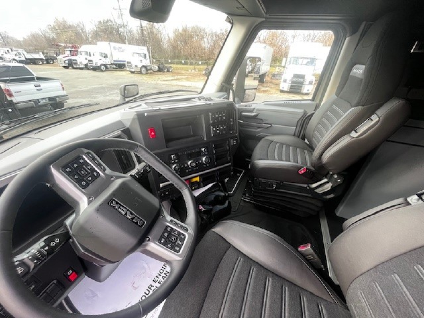 Truck cab interior of a 2026 Mack PR64T76M showing steering wheel, dashboard, and driver seat with controls and displays visible.