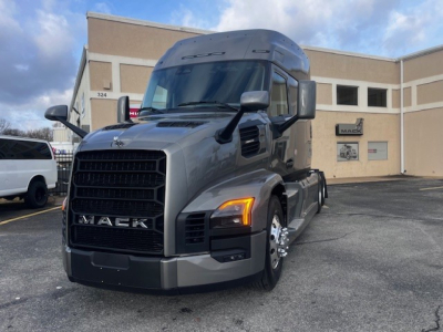 Front-left view of a new 2026 Mack PR64T76M tractor with gray paint, large grille, slim headlights, and chrome wheels.