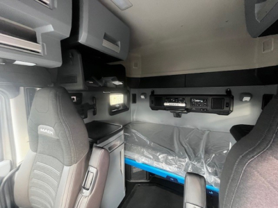 Cab interior of a new Mack PR64T76M sleeper tractor showing overhead cabinets, control panels, and a raised bunk with plastic cover; dashboard and seat backs visible.