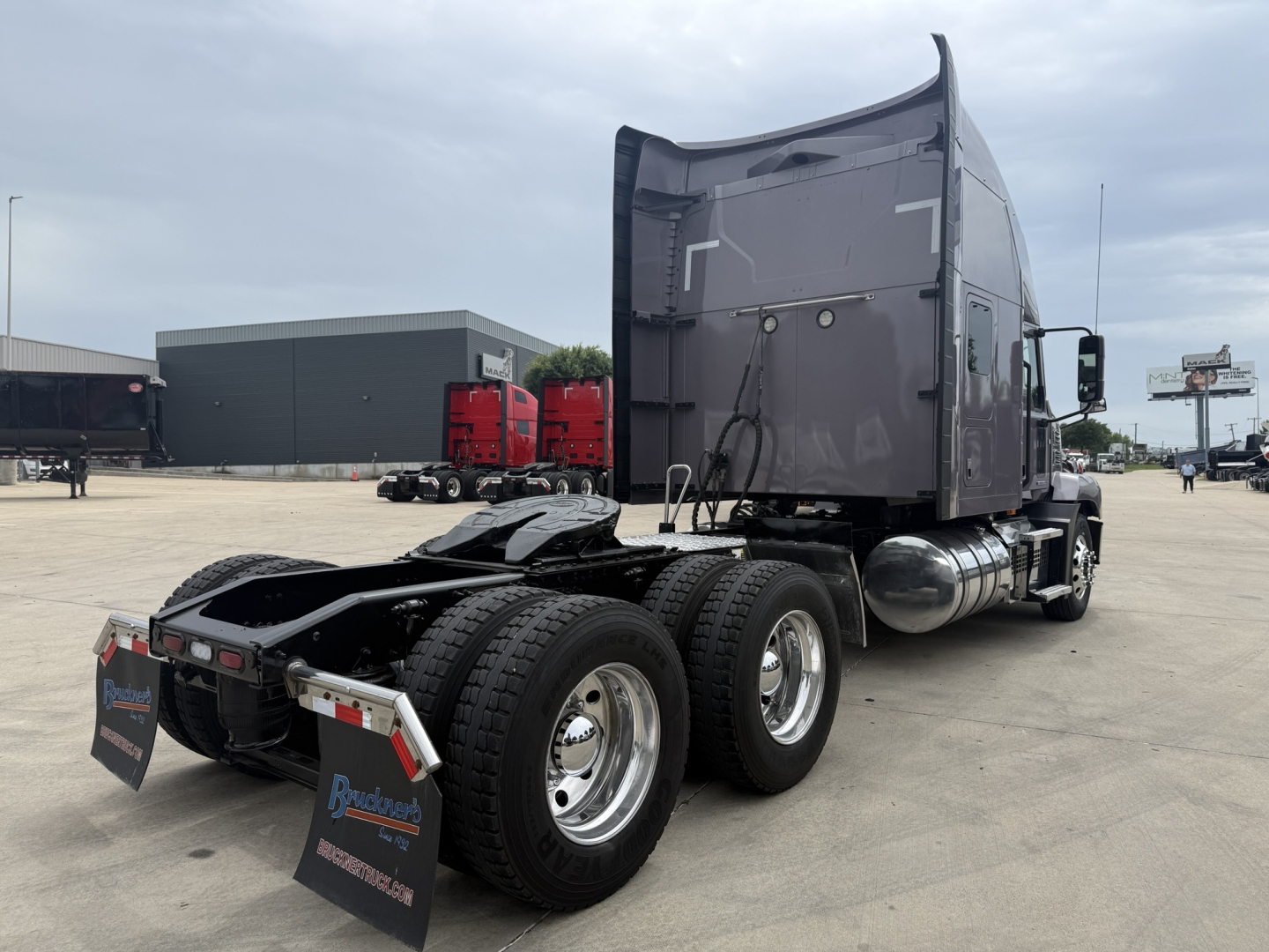 Truck chassis with semi-trailer rear, fuel tanks, and dual rear axles; sleeper cab visible in background.