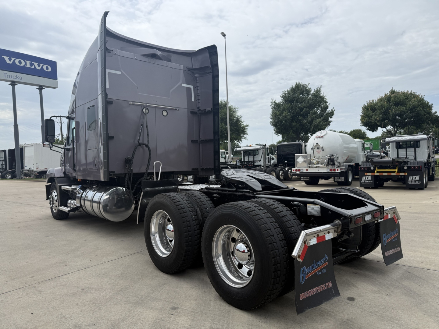 Truck cab and dual rear axles of a 2023 Mack AN64T70 tractor from a side-rear view, with fifth wheel and mud flaps, showing fuel tanks and exhaust.