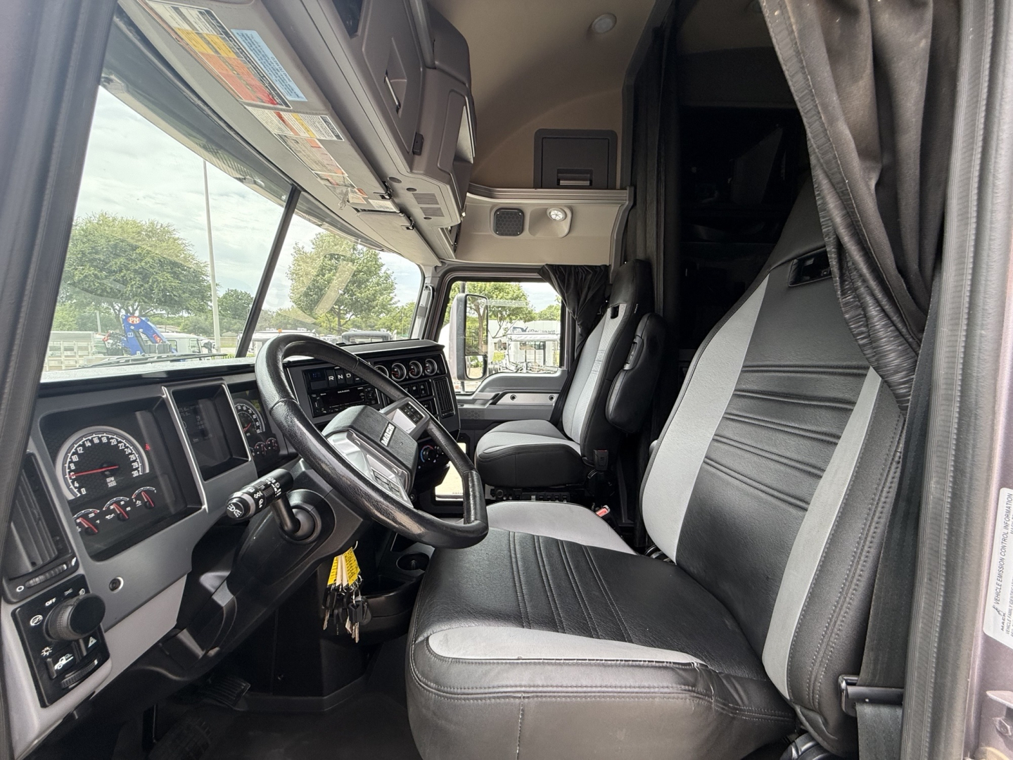 Truck cab interior showing steering wheel, dashboard, and driver seat of a Mack AN64T70 sleeper truck.