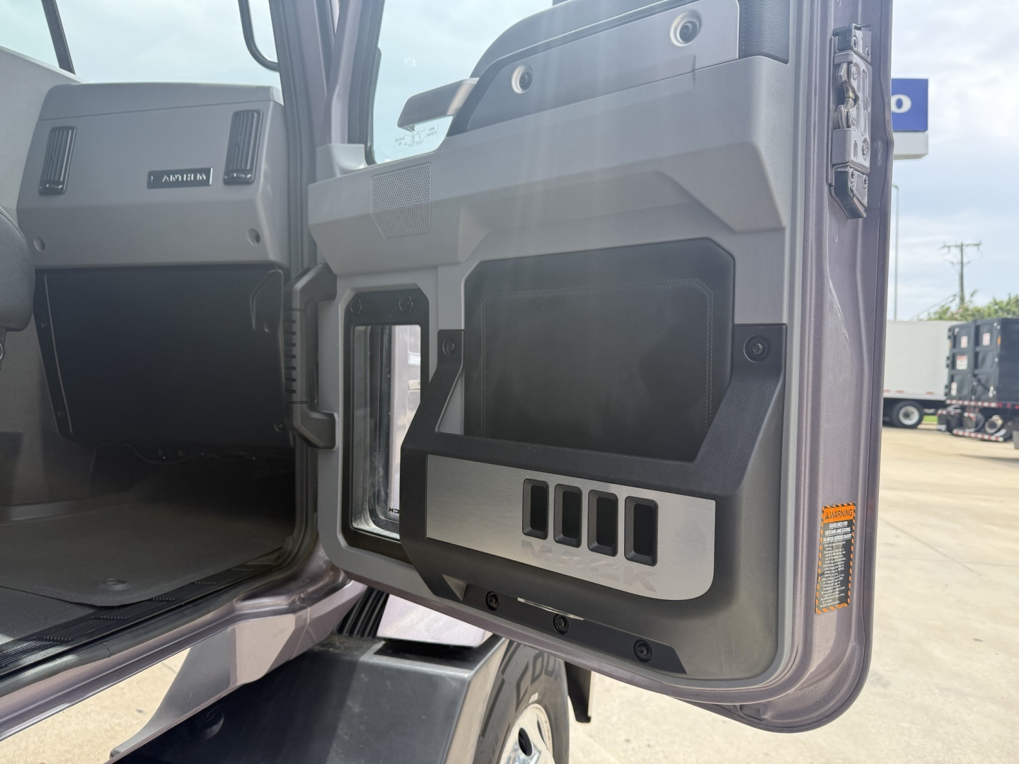 Truck cab door interior with storage pocket and control panels visible; door open showing dashboard area and steps; branding not legible.