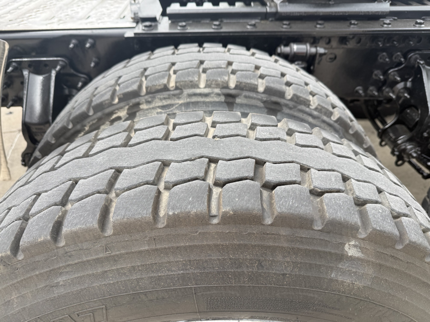 Truck tire close-up view under a Mack AN64T70 chassis showing heavy tread pattern and undercarriage components.