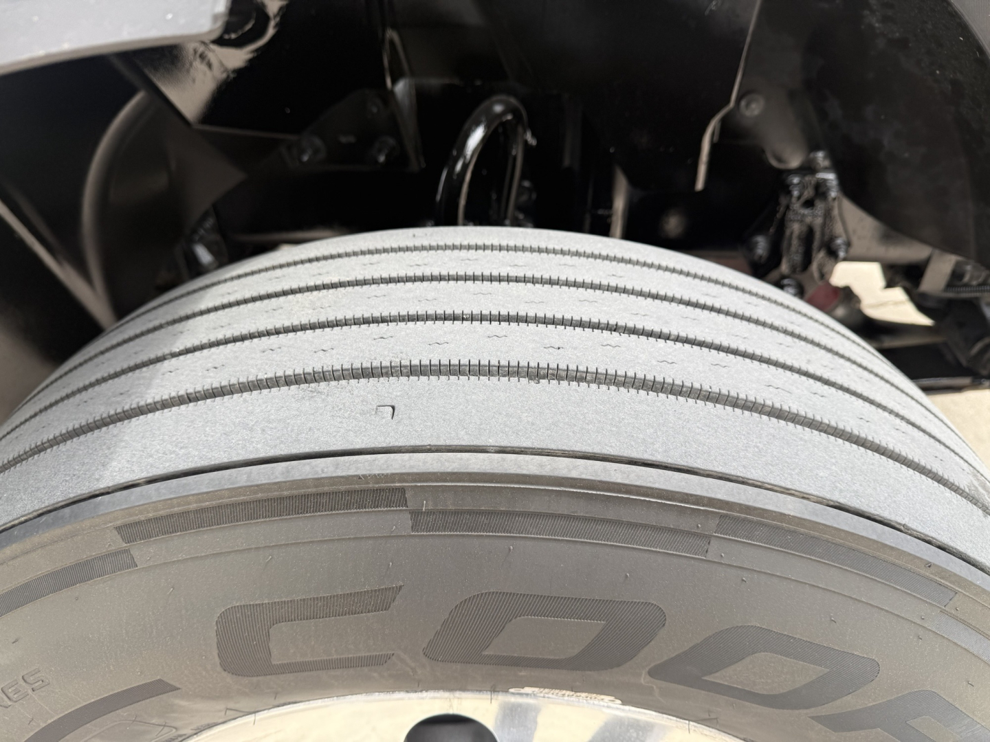 Truck wheel and fender area showing a close-up of a multi-plate treaded tire with partial undercarriage components visible.