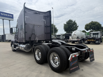 Truck cab and dual rear axles of a 2023 Mack AN64T70 tractor from a side-rear view, with fifth wheel and mud flaps, showing fuel tanks and exhaust.