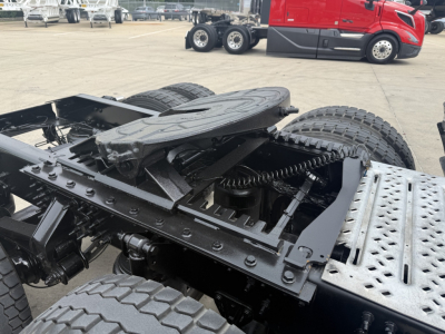 Truck chassis with fifth wheel and dual rear axles, exposed suspension and frame components, view of the drive area and fuel tank on a Mack AN64T70 listing.
