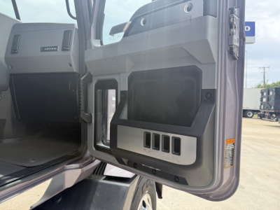 Truck cab door interior with storage pocket and control panels visible; door open showing dashboard area and steps; branding not legible.