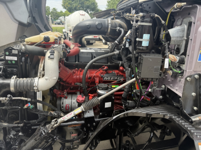 Mack AN64T70 engine bay showing red engine block and various hoses, belts, and wiring harnesses in the compartment.