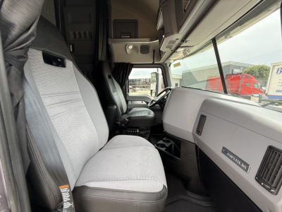 Inside of a Mack AN64T70 sleeper cab showing driver and passenger seats, dashboard, steering area, and seating upholstery.