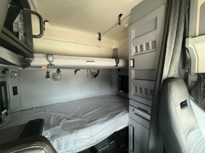 Truck sleeper cab interior with raised bunk bed area and storage compartments visible, including overhead cabinets and window shade.