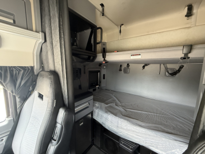 Sleeper cab interior of a 2023 Mack AN64T70 showing bunk area with mattress, overhead cabinets, control panel, and steel interior walls.