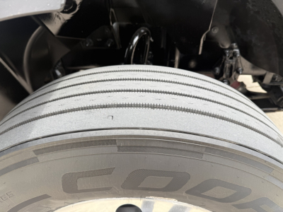 Truck wheel and fender area showing a close-up of a multi-plate treaded tire with partial undercarriage components visible.