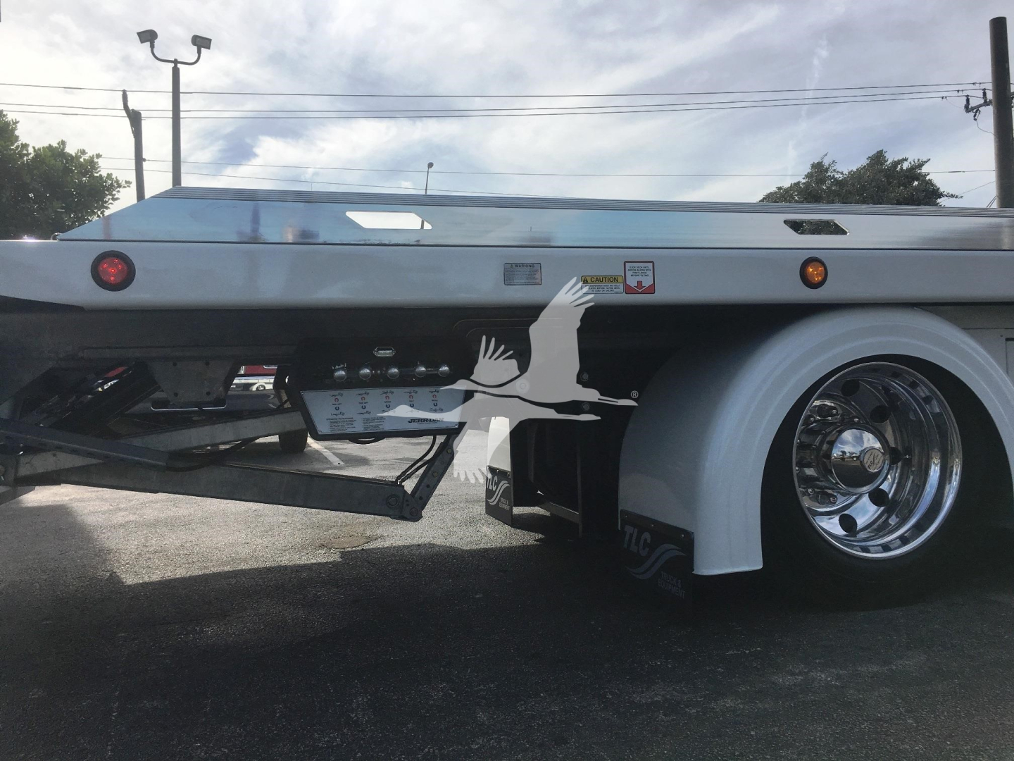 Truck rear/side view showing flatbed rollback equipment on a 2022 Peterbilt 337 with chrome wheel and white fender, concrete trailer hitch area visible.