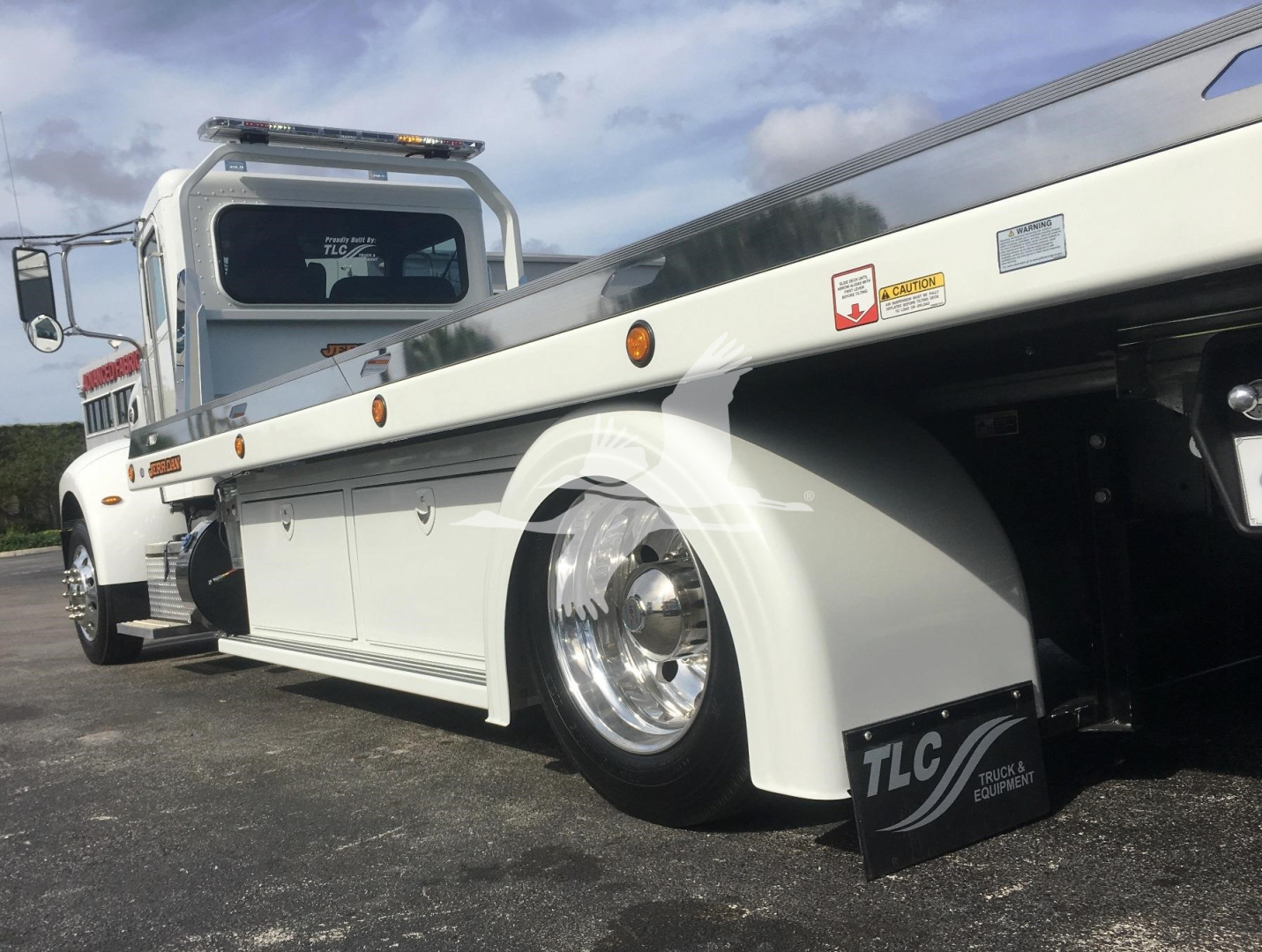 Truck bed and wheel of a 2022 Peterbilt 337 rollback with TLC Equipment sign visible