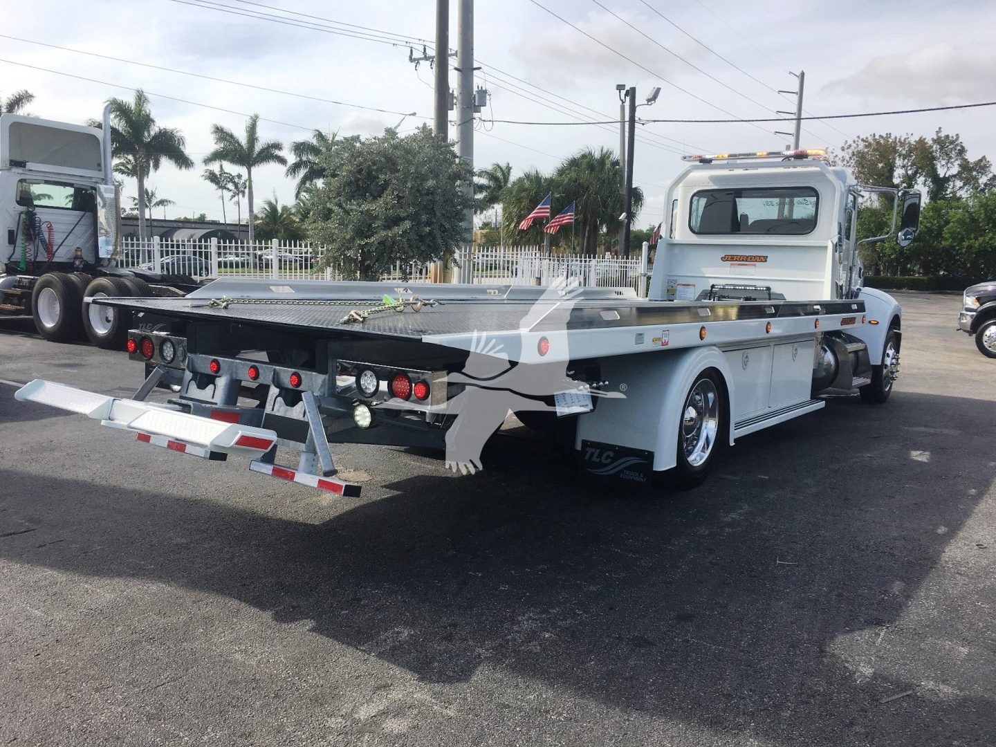 Peterbilt 337 rollback tow truck from rear-left angle showing flatbed and rear lights, with chain strap hooks and aluminum deck.