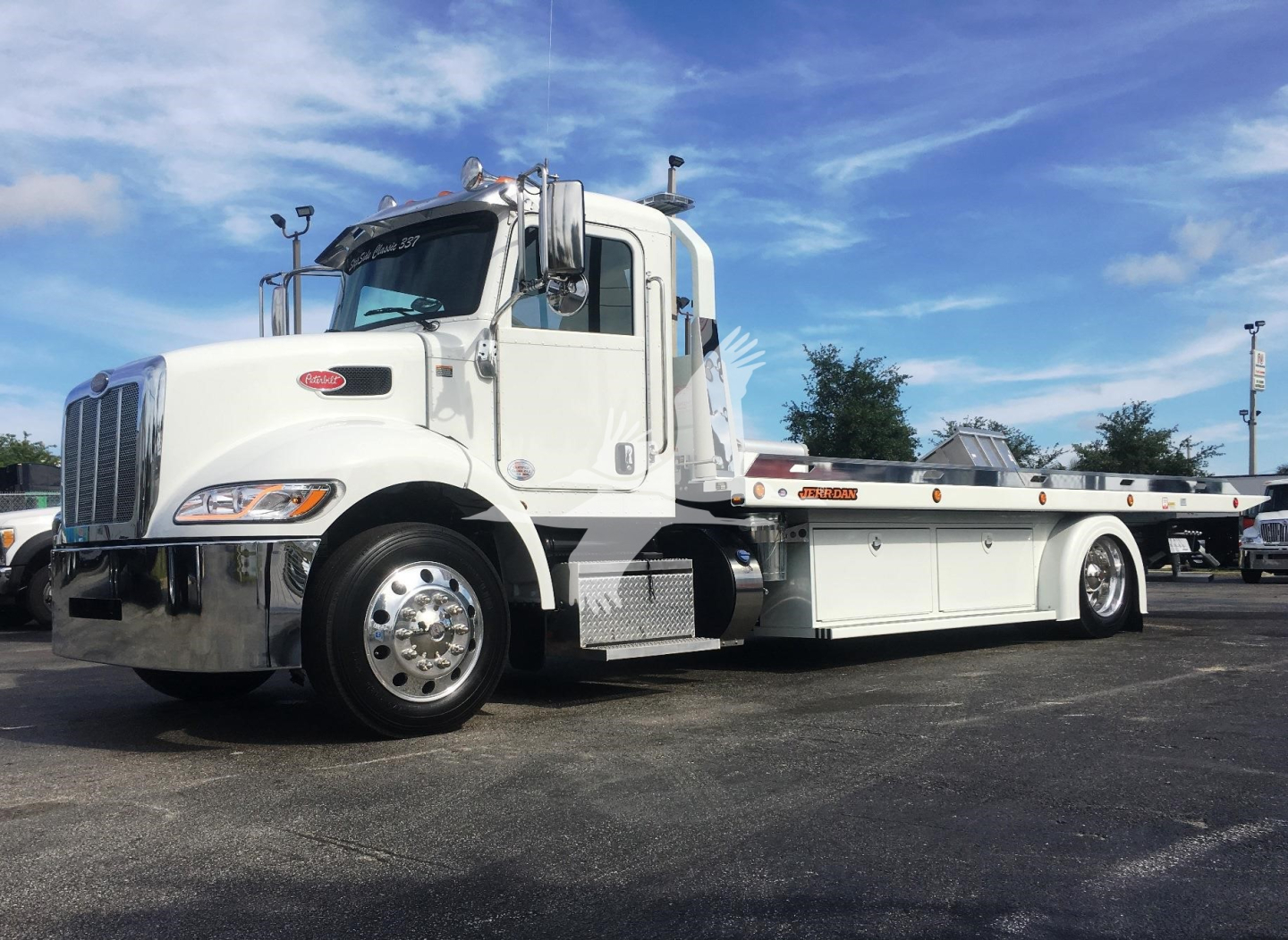 Peterbilt 337 rollback truck in white, side view showing long flatbed with toolboxes and chrome fuel tanks.