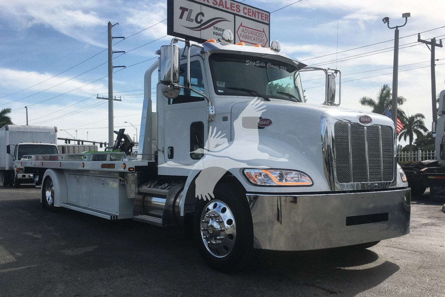 Peterbilt 337 rollback truck with chrome bumper and white paint. Front grille, two side mirrors, and a long flatbed are visible. No visible text legible on the truck from this angle.