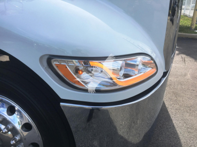 Truck headlight area of a 2022 Peterbilt 337 with chrome bumper and light housing; front fender and wheel visible.