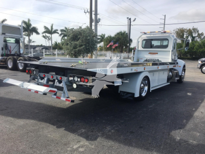 Peterbilt 337 rollback tow truck from rear-left angle showing flatbed and rear lights, with chain strap hooks and aluminum deck.