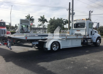 Peterbilt 337 rollback truck in a parking lot, side view showing flatbed with toolboxes, dual rear wheels, and chrome rims.