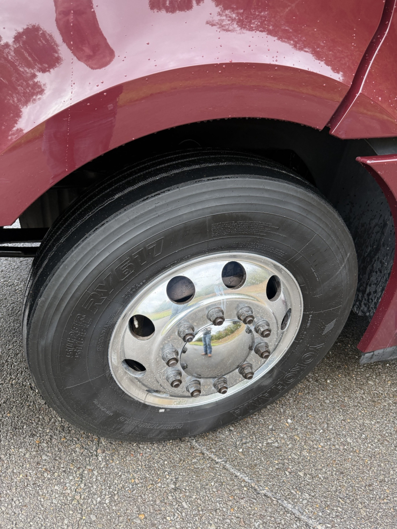 Freightliner Cascadia 126 front wheel and fender showing steel wheel with lug nuts and tire; maroon truck body above the wheel.