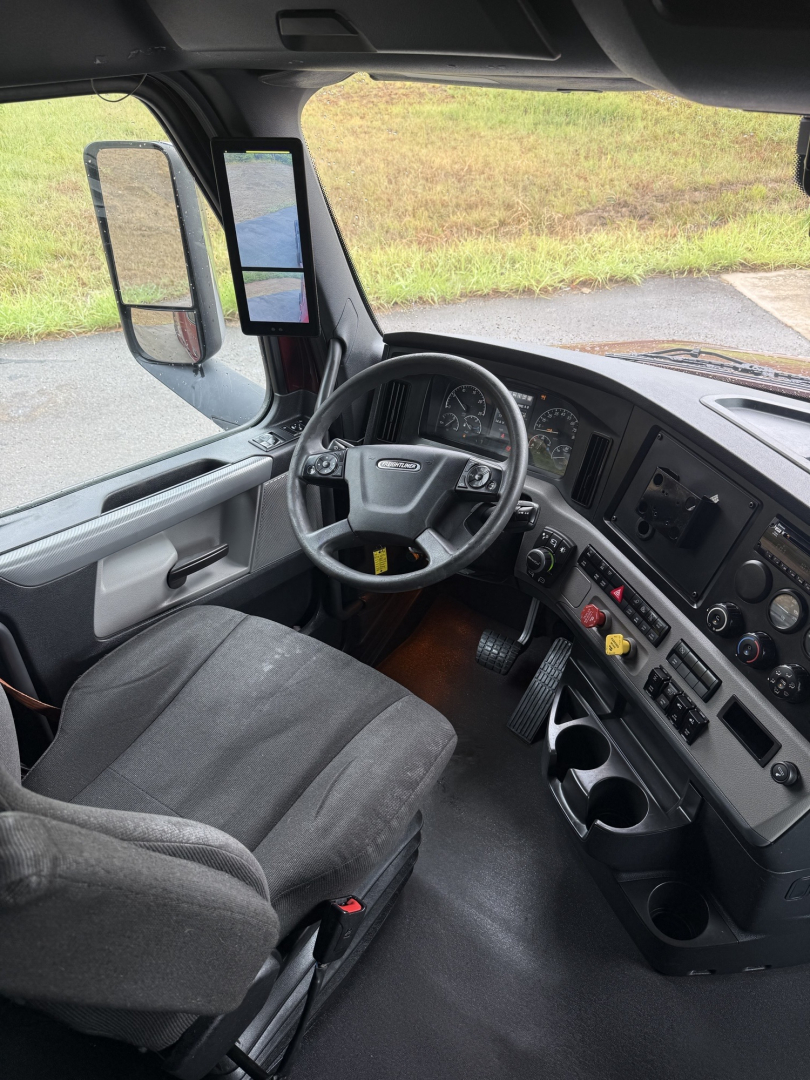 Interior cabin with steering wheel, dashboard, and driver seat of a Freightliner Cascadia 126 truck showing gauges, control panel, and side mirror.
