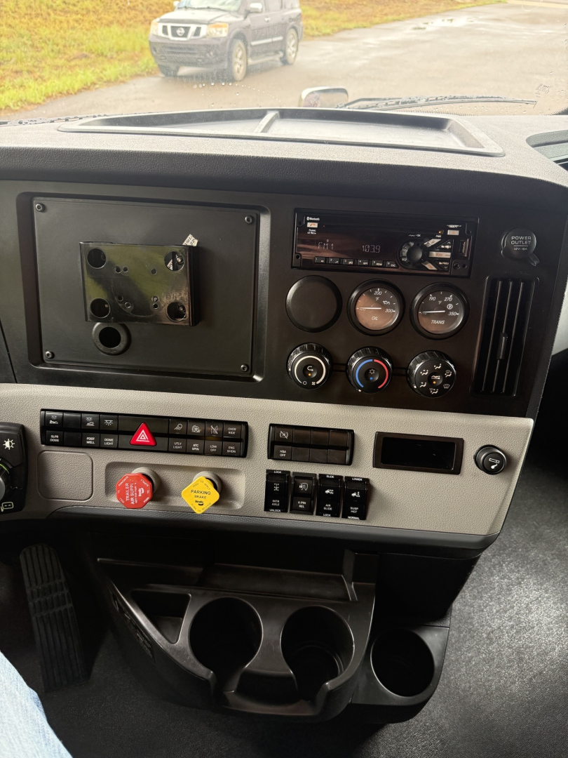 Dashboard of a Freightliner Cascadia126 truck showing control dials, switches, and cup holders; no visible model labels or badge text identifiable.