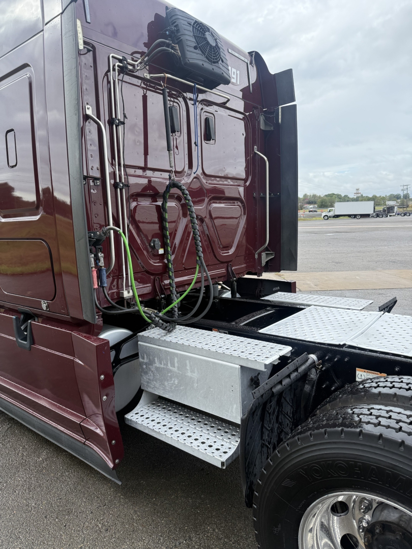 Truck cab rear view showing aluminum step and green hoses, maroon Freightliner Cascadia 126 sleeper truck. visible tires and air/electrical lines near rear doors.