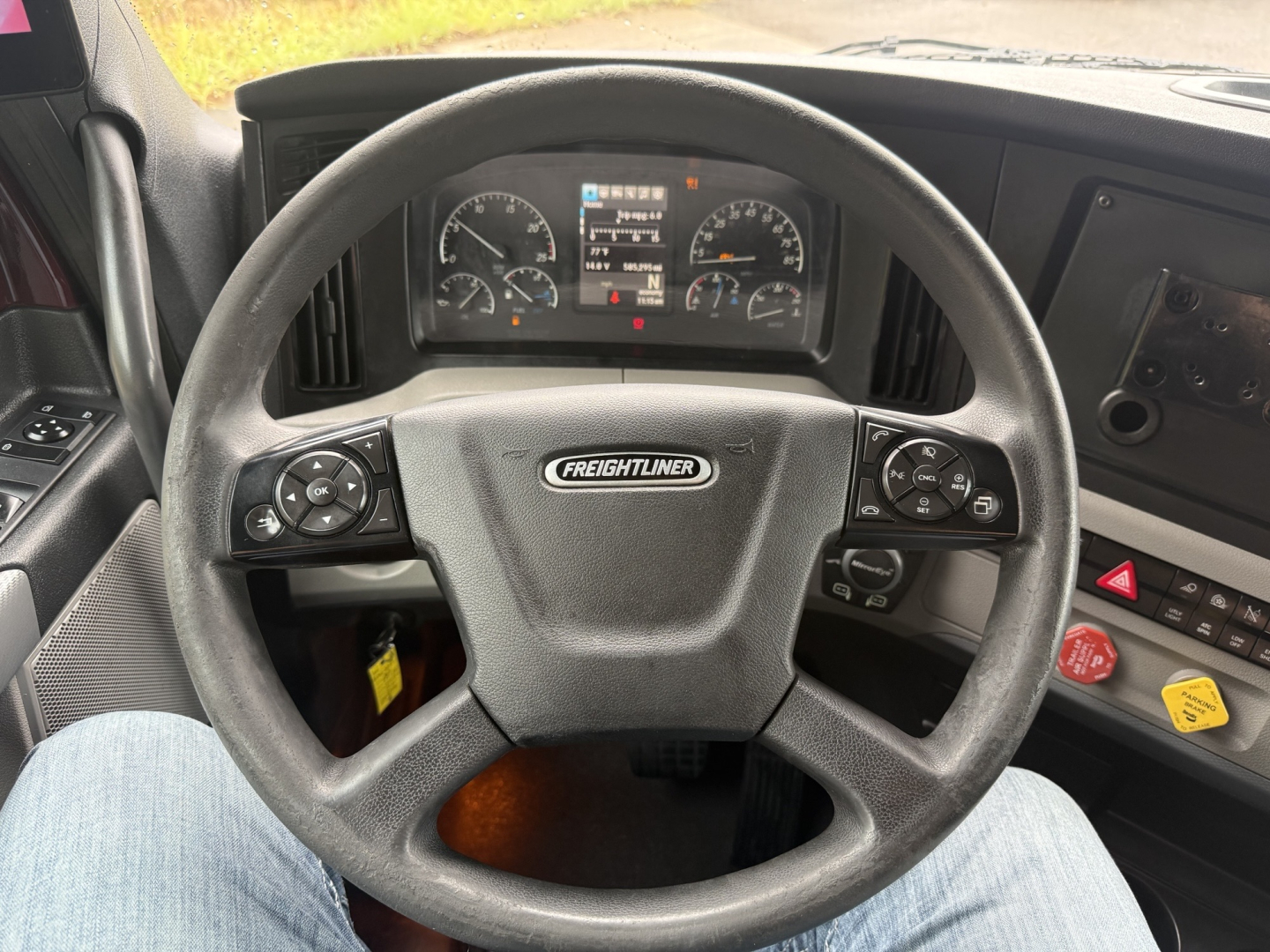 Steering wheel area of a Freightliner Cascadia dashboard with instrument cluster and controls visible.