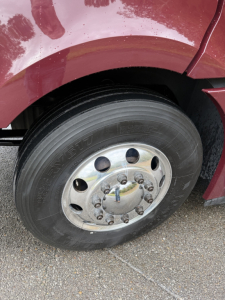 Freightliner Cascadia 126 front wheel and fender showing steel wheel with lug nuts and tire; maroon truck body above the wheel.