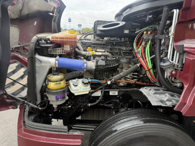 Freightliner Cascadia 126 engine bay showing coolant reservoir, blue silicone hose, multiple colored wiring harnesses, and auxiliary components.