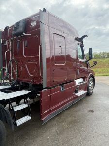 Truck side view showing cab and rear sleeper area of a maroon 2021 Freightliner Cascadia 126 with external steps and side panel details.