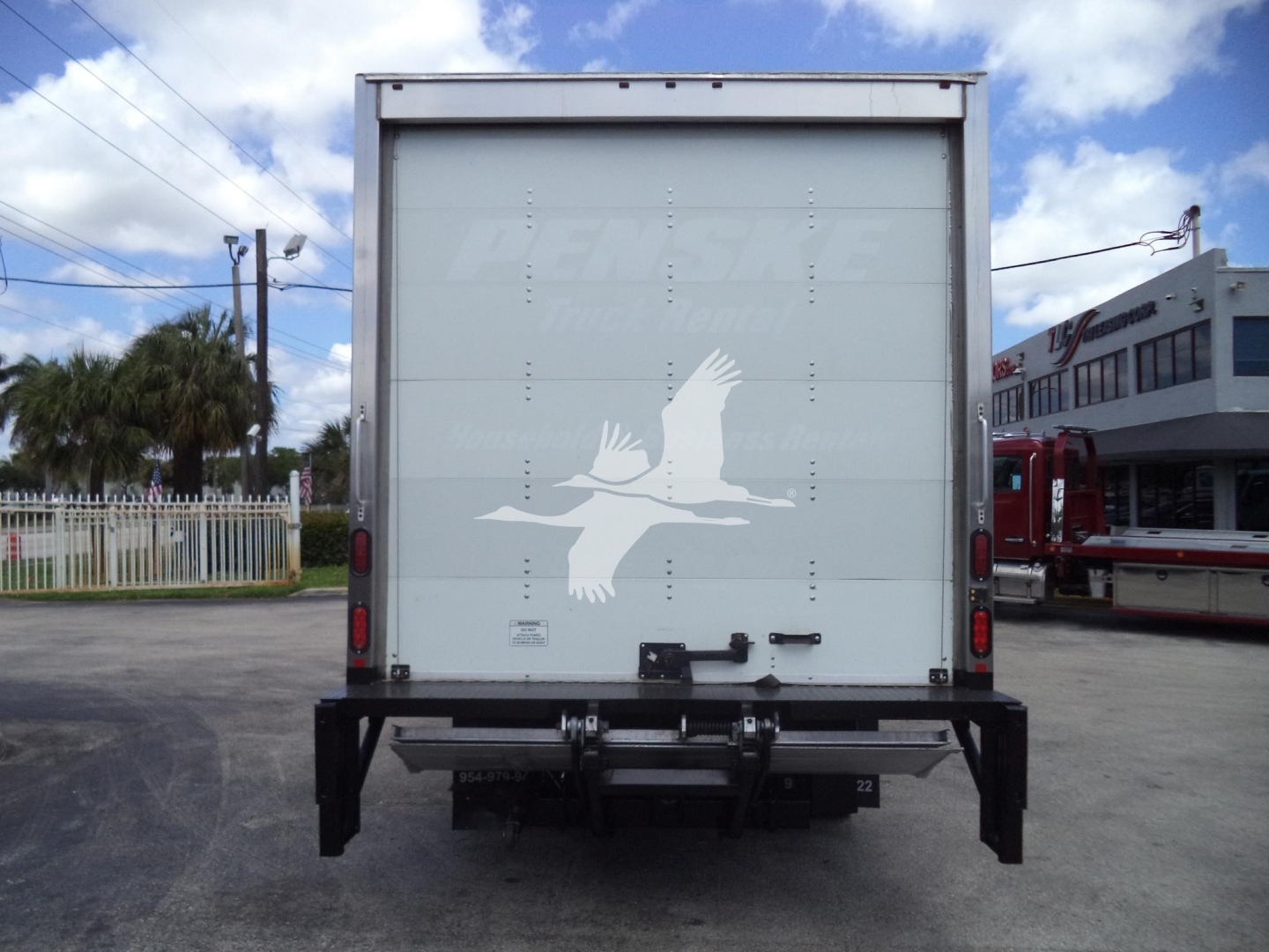 Isuzu NPR box truck rear view showing raised logo on rear door and tail lift platform.