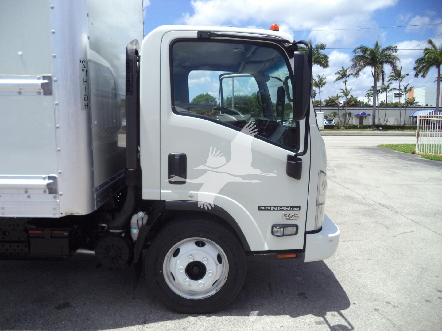 Isuzu NPRHD cab front left view showing side mirror and windshield, with cargo box attached.