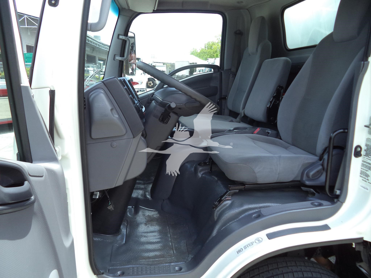 Isuzu NPR-HD truck cab interior showing driver and passenger seats, dashboard, steering wheel, and floor mat from side open door.