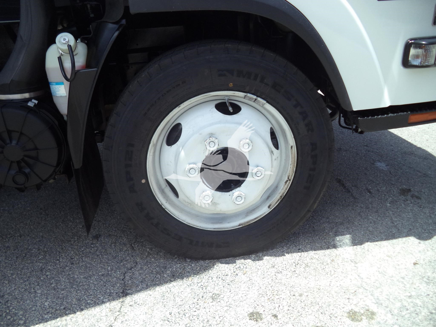 Isuzu NPR HD front wheel area showing tire, rim, and part of the front fender and lamp; visible markings on tire read 'NIT...' and some vehicle components like brake lines and reservoir.