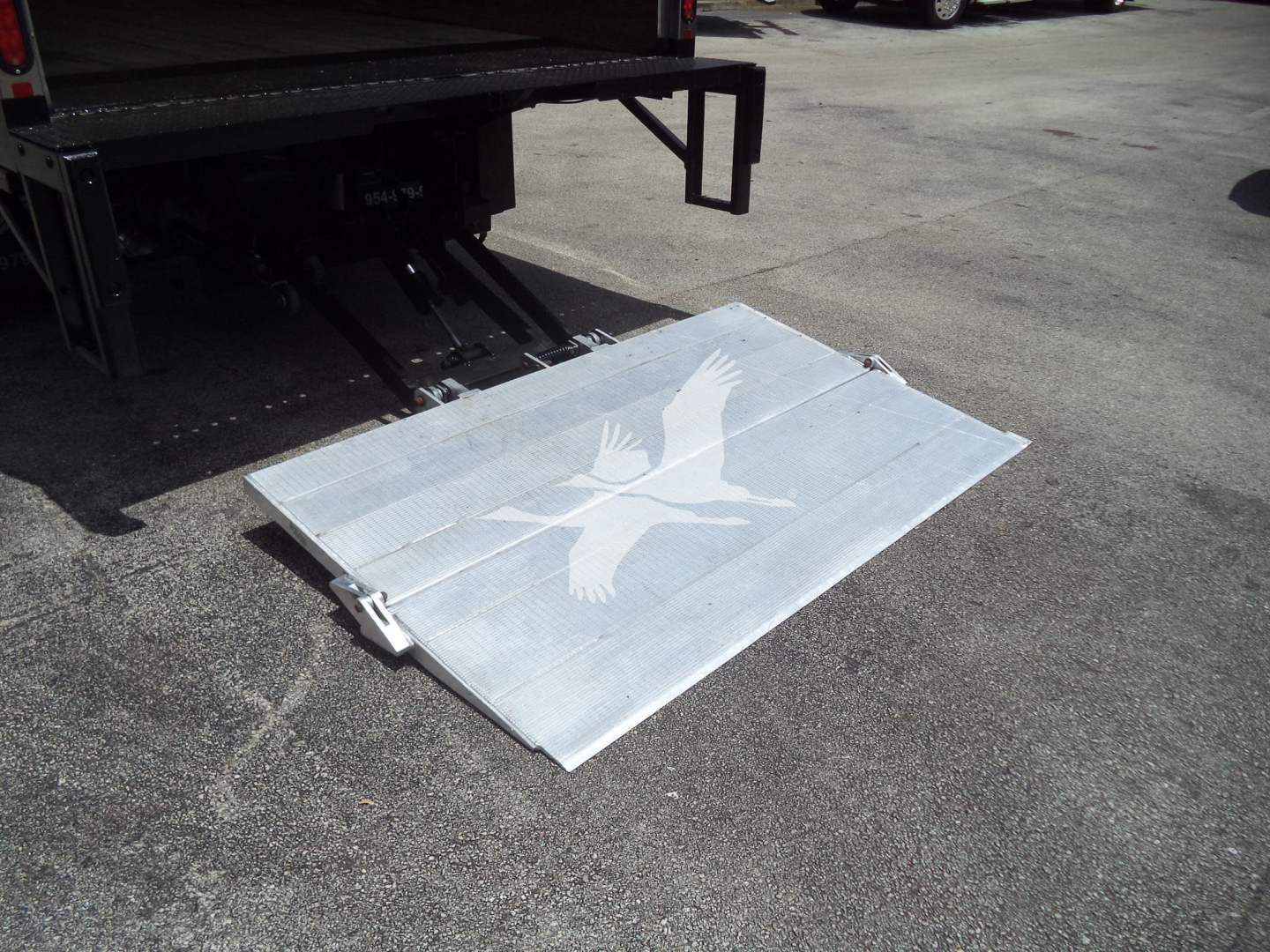 Aluminum ramp or step with a white bird logo placed on ground near Isuzu NPR HD truck bed hoist area.