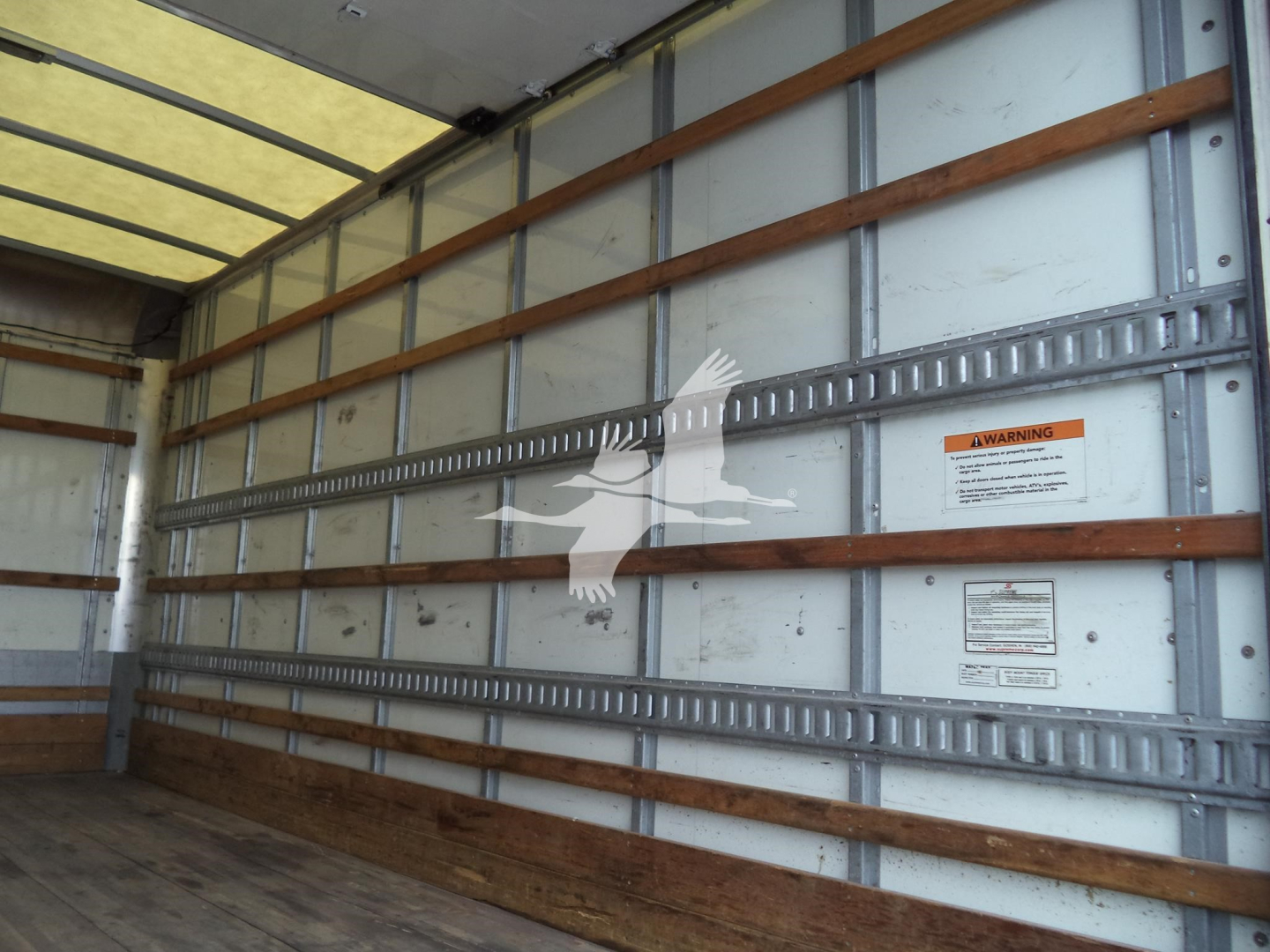 Truck cargo area with wooden side rails and metal track, inner wall with warning label and small stickers.